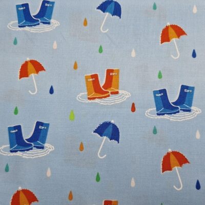 Tela de algodón tipo patchwork, de fondo azul claro, con dibujos de katiuskas y paraguas azules y naranjas con gotas de lluvia de colores