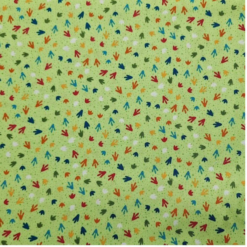 Tela de algodón verde con estampado menudo de huellas de dinosaurio en colores rojo, azul y naranja de la colección Dino Friends de Makower.