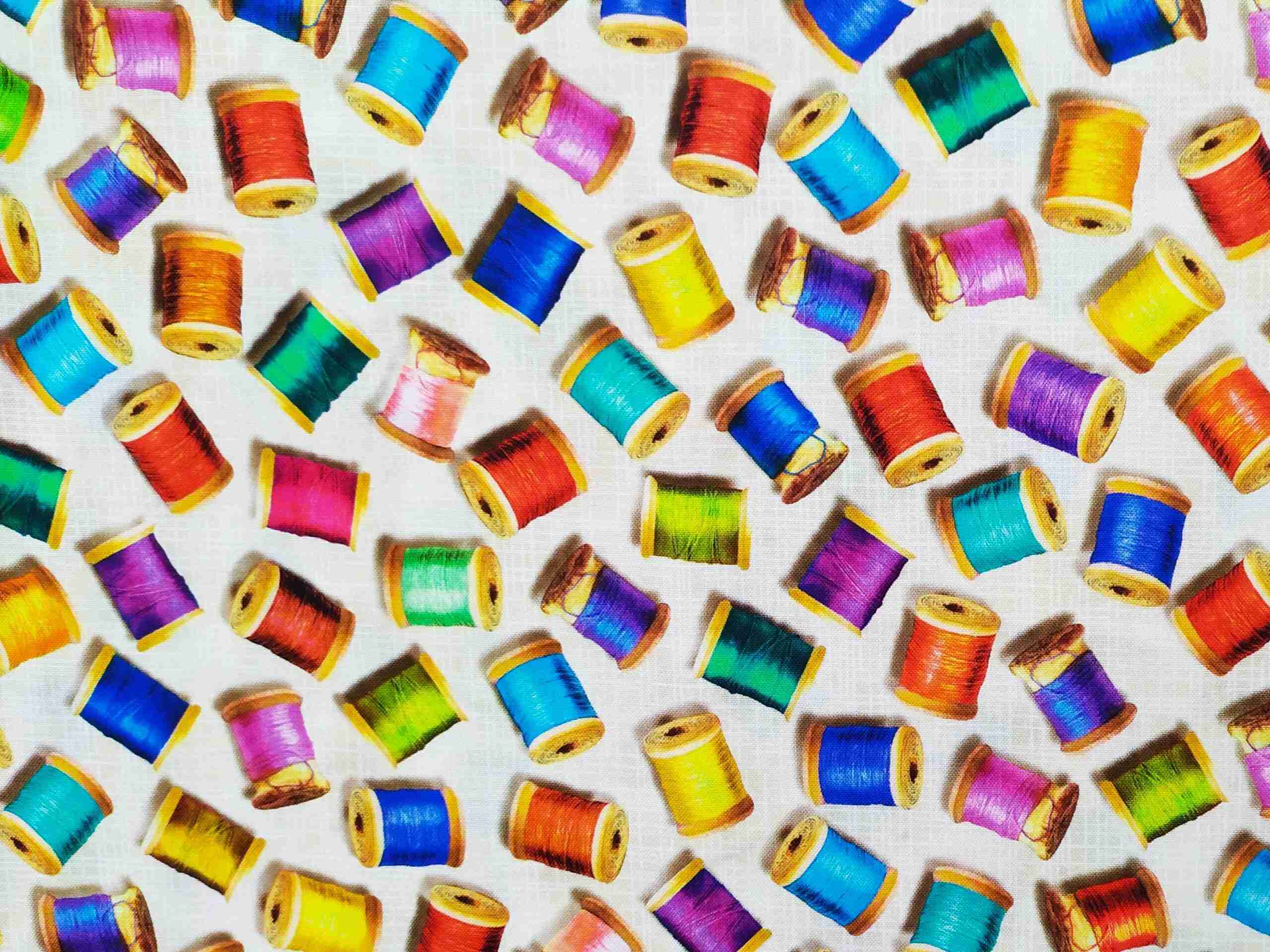 Tela de patchwork con estampado de carretes de hilos de colores sobre fondo blanco roto de la colección Sewing Emporium de Robert Kaufman.